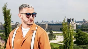Jeune homme à Paris portant lunettes de soleil et veste orange.