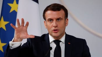 Emmanuel Macron en discours avec drapeaux français et européen en arrière-plan.