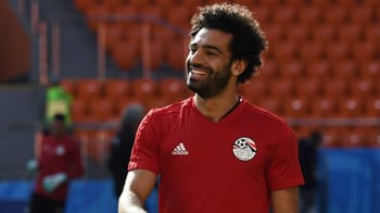 Footballeur africain portant maillot rouge dans un stade vide.