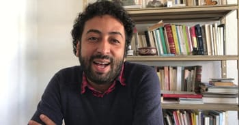 Homme souriant avec bibliothèque en arrière-plan.