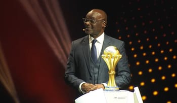 Homme en costume avec trophée de football sur scène.