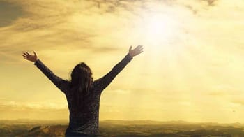 Personne avec les bras levés regardant le soleil couchant.