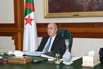Homme politique algérien lors d'une réunion officielle avec drapeau national en arrière-plan.