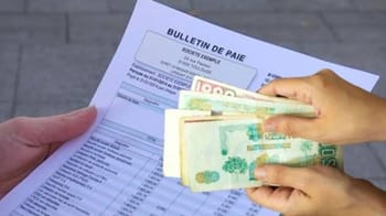 Main tenant des billets de banque et un bulletin de paie sur une table.