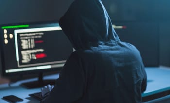 Hacker en hoodie travaillant sur un ordinateur avec code informatique.