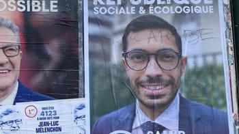 Portrait d'un candidat politique avec lunettes et costume bleu.