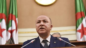Homme politique lors de la réunion du gouvernement, drapeaux algériens en arrière-plan.