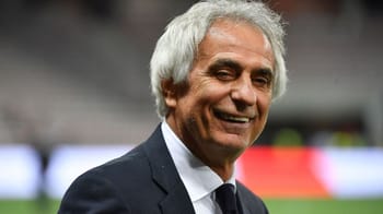 Homme d'âge moyen en costume souriant lors d'un match de football.