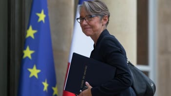 Elisabeth Borne avec un dossier officiel, souriante, devant un drapeau européen.