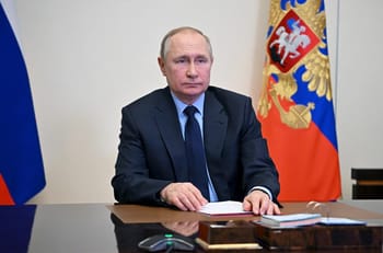 Vladimir Poutine assis à une table avec drapeaux russes en arrière-plan.