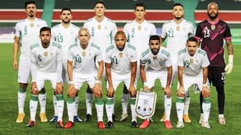 Groupe de joueurs de football algériens en tenue blanche sur le terrain.