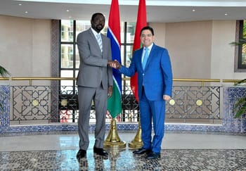 Deux hommes en costume se serrent la main devant les drapeaux du Maroc et de la Gambie.