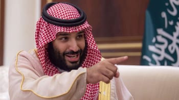 Homme saoudien en tenue traditionnelle souriant et pointant du doigt.