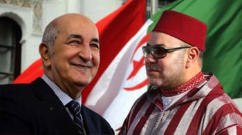 Deux hommes en discussion avec drapeaux algérien et marocain en arrière-plan.