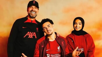 Photo de trois personnes, deux hommes et une femme, en vêtements de Liverpool FC.