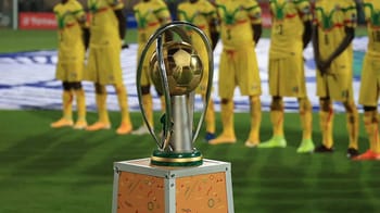 Trophée de la CAN 2023 avec équipe en arrière-plan.