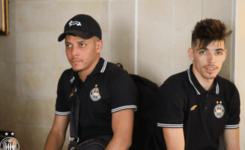 Deux jeunes joueurs de football assis, portant des maillots noirs avec logo.