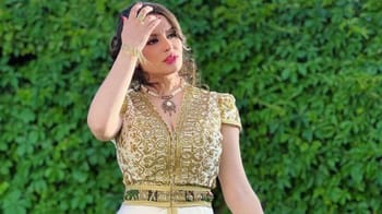 Halyma Alma en tenue chic avec un fond de verdure luxuriante.