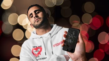 Riyad Mahrez tenant un téléphone cassé, expression sérieuse.