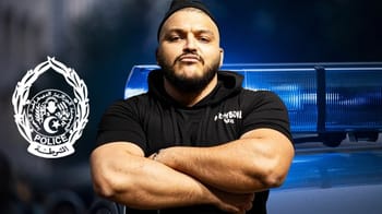 Rappeur Trap King avec bras croisés devant une voiture de police.
