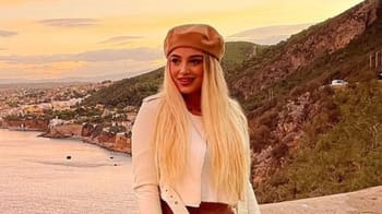 Jeune femme blonde souriante avec paysage de montagne et mer en arrière-plan.