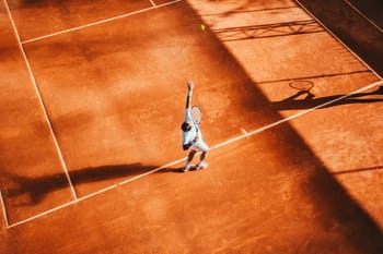Joueur de tennis sur court en terre battue avec ombres.