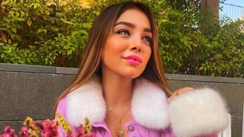 Jeune femme souriante avec veste en peluche rose et collier doré.