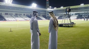 Deux femmes en abaya regardent un match de football au stade.