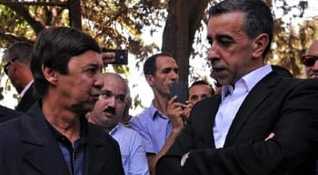 Deux hommes en discussion lors du procès, entourés de témoins et de médias.