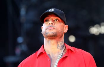 Booba portant un chapeau noir et une chemise rouge lors d'un événement.