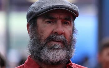 Eric Cantona avec un chapeau gris et une barbe fournie.