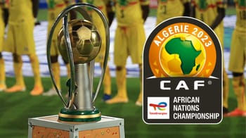Trophée de la CAN 2023 avec équipe de football en arrière-plan.