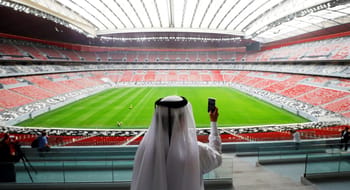 Spectateur en tenue traditionnelle regardant le stade vide au Qatar.