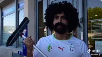 Humoriste avec perruque afro et canne, expression moqueuse.