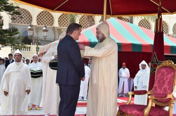 Homme en costume et homme en tenue traditionnelle lors d'une cérémonie.