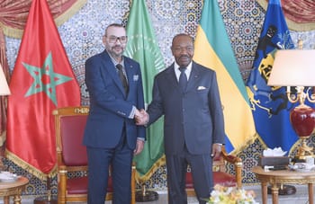 Deux hommes en costume se serrent la main devant des drapeaux africains et marocains.
