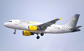 Avion Vueling blanc avec logo jaune en vol dans le ciel gris.