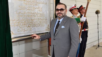 Homme en costume gris et lunettes de soleil lors d'une cérémonie officielle.