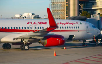 Avion Air Algérie stationné à l'aéroport avec bâtiments modernes en arrière-plan.