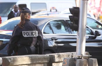 Policière en uniforme à côté d'une voiture noire sur une rue urbaine.