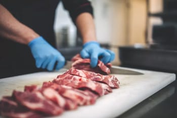Préparateur de viande avec des gants bleus coupant de la viande fraîche.