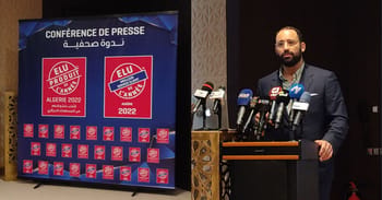 Homme parlant lors d'une conférence de presse avec logo ELU 2022 en arrière-plan.