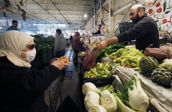 Vendeur de légumes vendant des artichauts et poivrons à une cliente au marché.