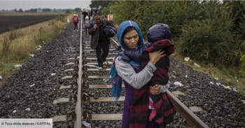 Famille migrante traversant des voies ferrées en zone rurale.