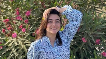 Inès Abdelli souriante dans un jardin avec des fleurs roses et vertes.