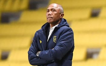 Homme d'entraînement de football marocain en veste bleue dans un stade vide.