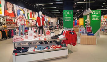 Vitrine d'un magasin de vêtements avec mannequins et rayons colorés.