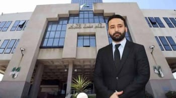 Nassim Diafat en costume devant un bâtiment officiel en Algérie.