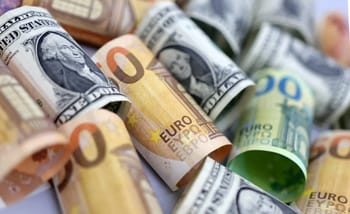 Foule de billets de banque en euros et dollars enroulés et dispersés.