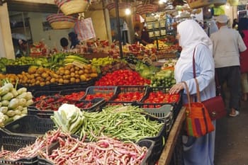 Vendeuse dans un marché algérien avec étalage de fruits et légumes frais.